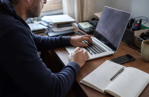 A small business owner working at a laptop with a mobile phone and a job diary on the desk beside them.