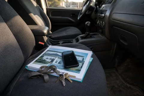 A cell phone showing missed calls resting on a folder of property details on a car passenger seat