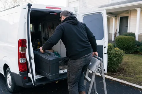 A locksmith loading tools into a sign-written van outside an American house at the start of the working day